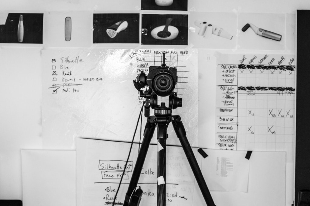 A DSLR camera mounted on a tripod stand in front of a whiteboard on which rough photography workflow is mentioned
