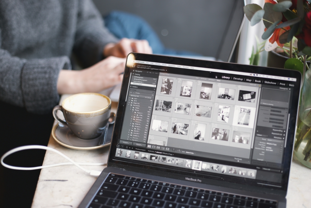 Saving and backing up photographs in Lightroom on a laptop placed on a tabletop alongside a coffee mug