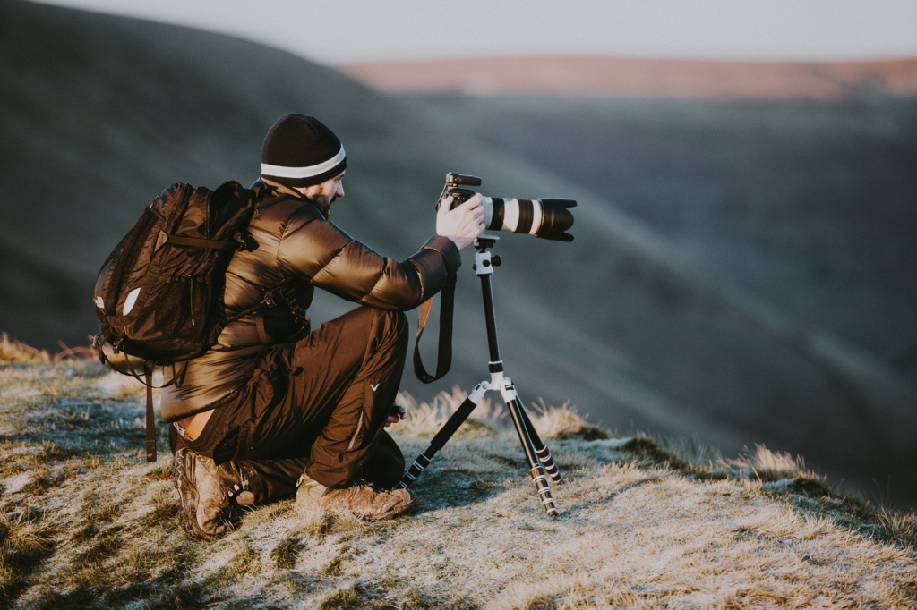 A landscape photographer mounting a camera on a tripod on top of a cliff