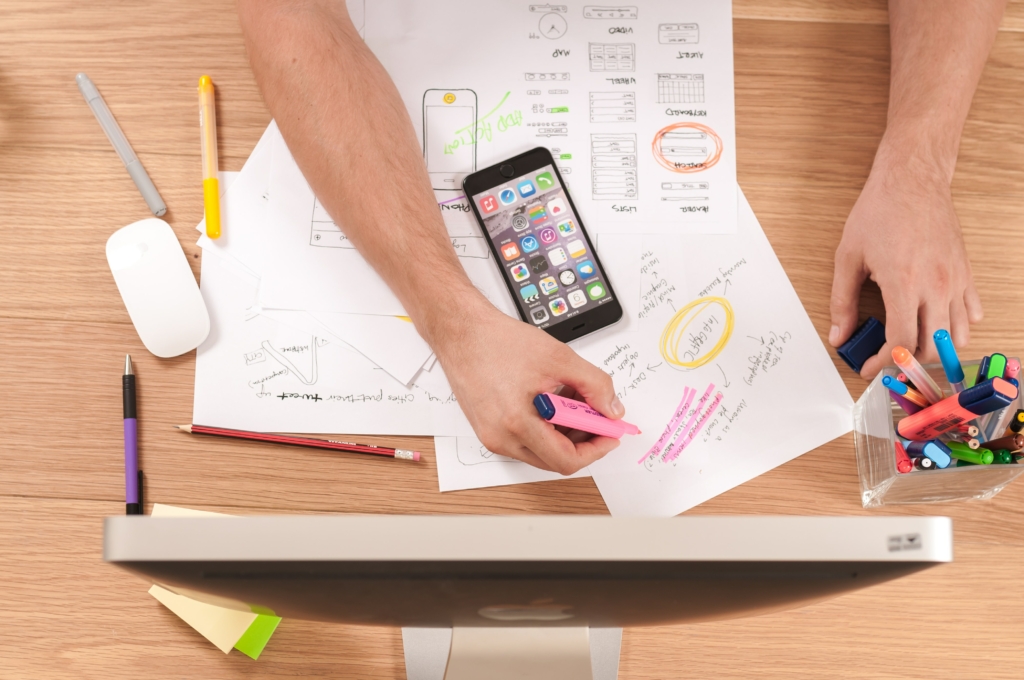 Bird's-eye view of a table top with multiple papers, pens, and iMac