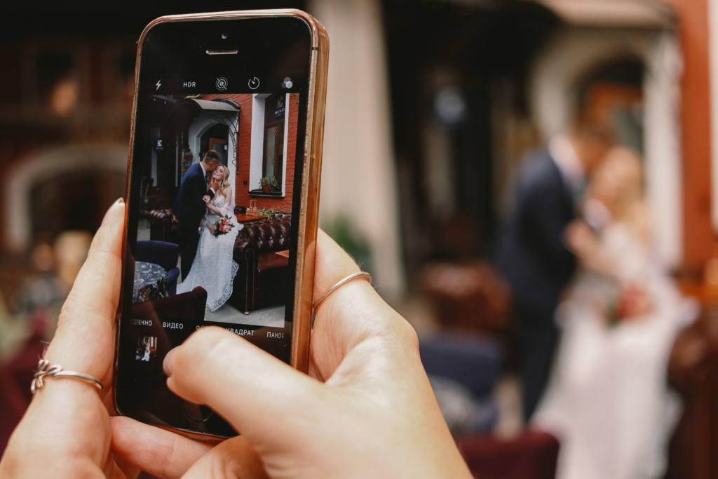 A person capturing a photo of a bride and groom through their phone