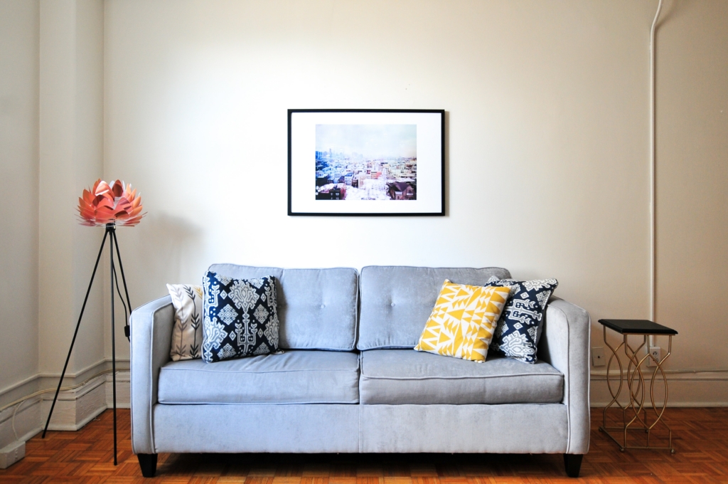 A grey-colored sofa placed at the center with a framed picture on the wall behind