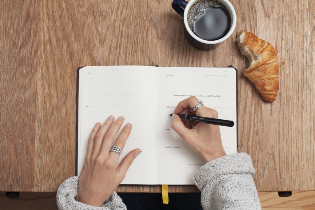 A person working on a planner with a coffee mug and a croissant at the side